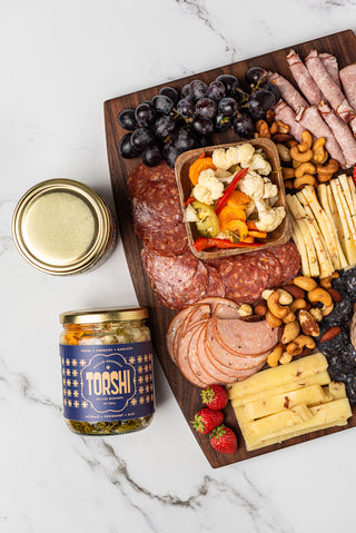 Torshi jar beside a charcuterie board with a bowl of pickled vegetables